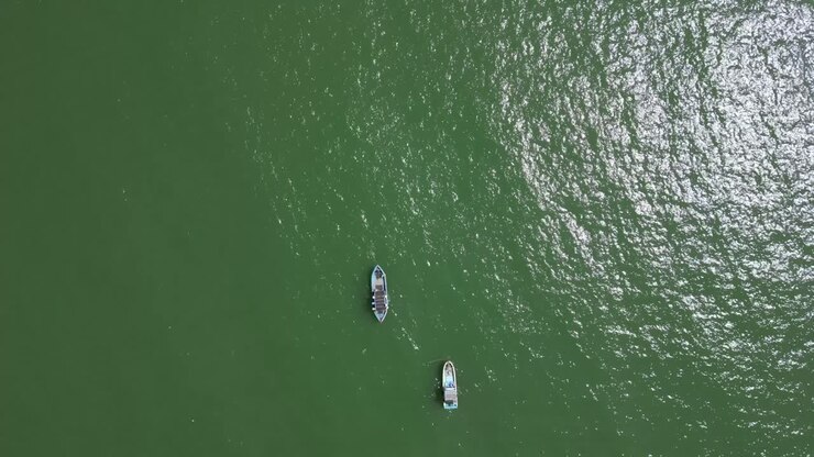 Two fishing boats flying over wide open ocean, top down drone tracking shot