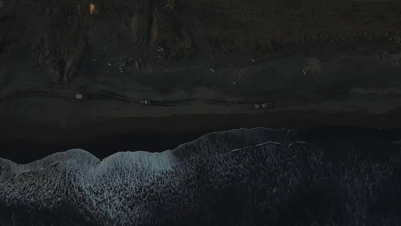 вид с высоты птичьего полета, перспектива сверху, съемка с дрона с воздуха волн, разбивающихся о берег, машин, едущих по черному песку в сан-хосе, гватемала