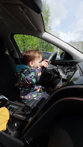 small cute boy playing in car. steering wheel playful child. vertical video.