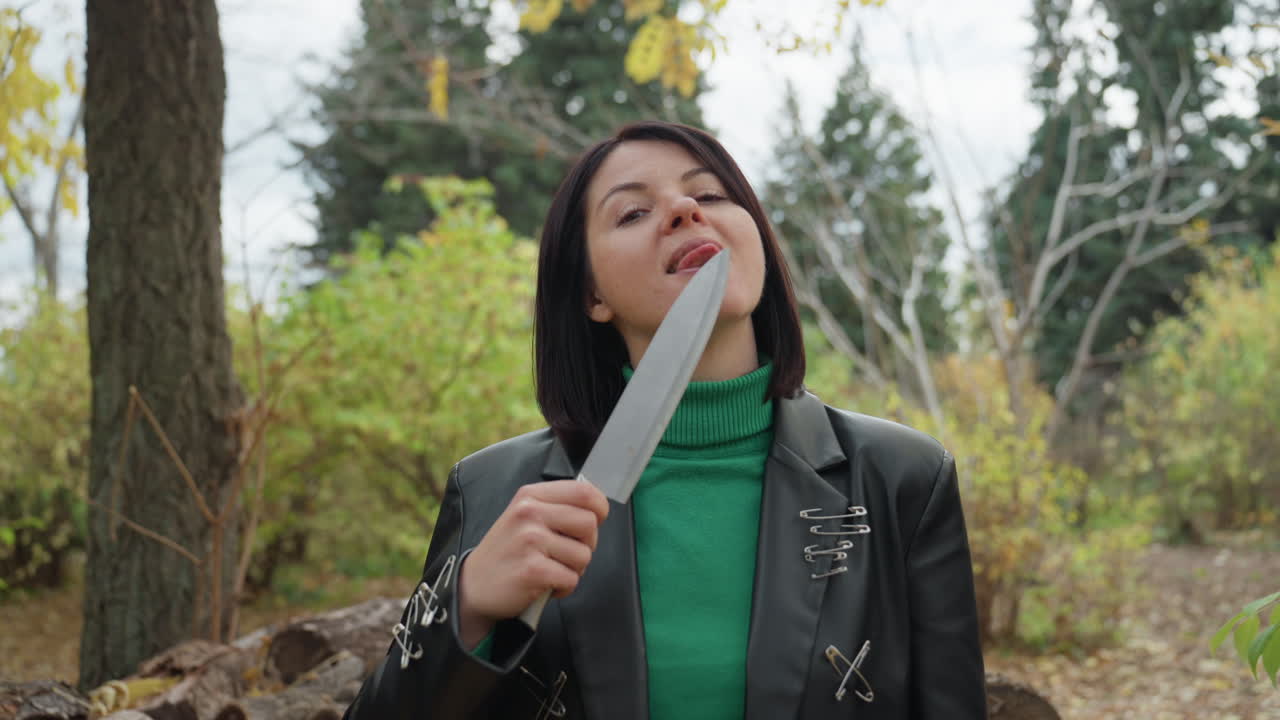 Eine selbstbewusste Frau, die ein Messer untersucht, Herbstwaldszene mit einer Frau, die eine Klinge inspiziert, Herbstwald-Hintergrund, während eine Frau in Lederkleidung ihr Messer mit einem selbstsicheren Ausdruck genauestens untersucht