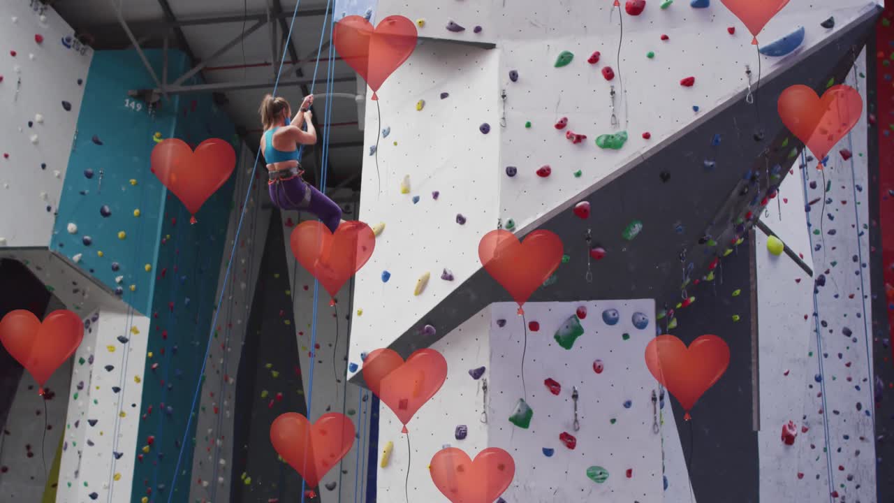 globos rojos en forma de corazón flotando contra la pared de una mujer en forma caucásica escalando en el gimnasio