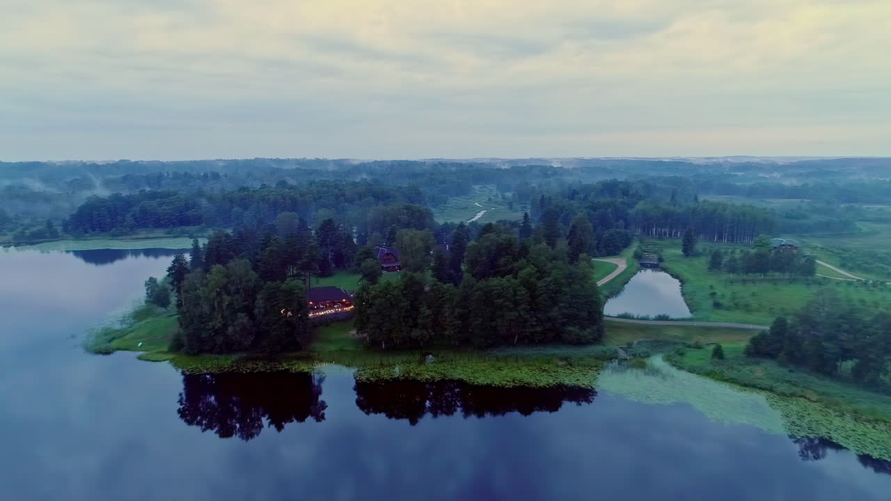 흐린 날 반 섬에 있는 나무로 둘러싸인 집의 아름다운 공중과 모든 것이 고요한 호수에 반사되고 있습니다.