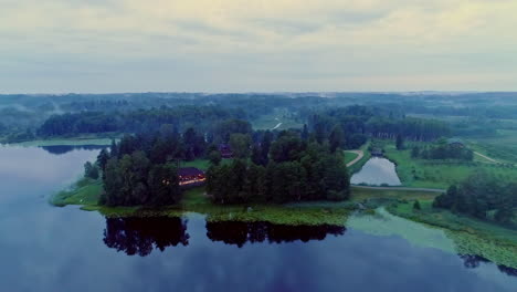 beautiful aerial of a house surrounded by trees on a half island on a cloudy day with everything being mirrored in the still lake