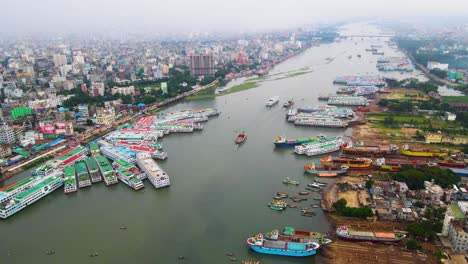 aerial over dhaka city’s ship terminal on buriganga river port, revealing numerous ships and the city skyline, with a misty sky from pollution.