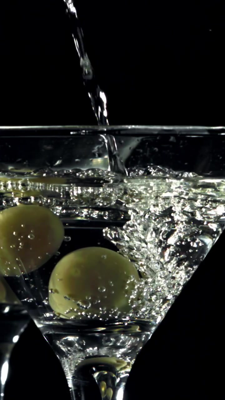 Versamento al rallentatore di Martini con olive in un bicchiere