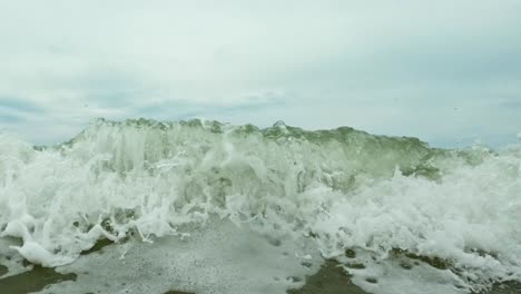 Slow-motion-of-an-incoming-wave,-touching-the-cameras-lense,-lower-view-from-the-sea-level