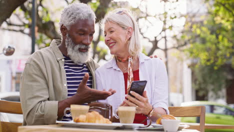 older couple enjoying a cafe breakfast while using a mobile phone