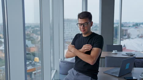 smiling confident young businessman in the light office. man puts on glasses looking into camera. blurred backdrop.