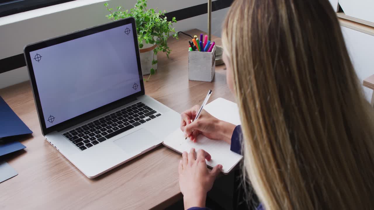 Caucasian businesswoman taking notes during video call, using laptop with copy space on screen