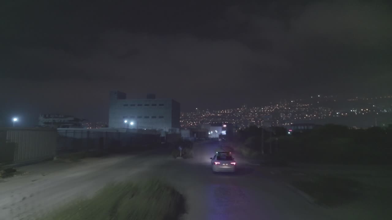 Night aerial footage of a police car driving down a dark urban area