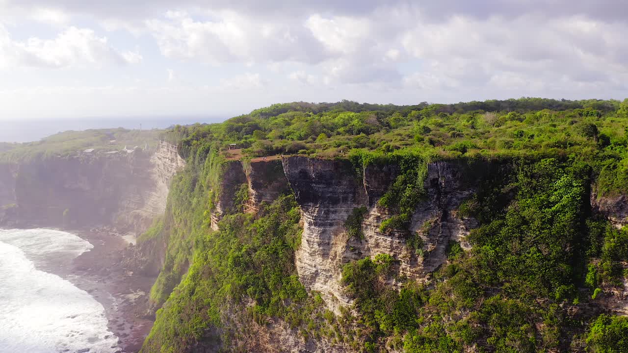 acantilados de uluwatu, vista aérea que revela el acantilado de borde afilado con un exuberante paisaje verde, capas de piedra caliza terciaria y olas del océano índico rompiendo en la playa, bali, indonesia
