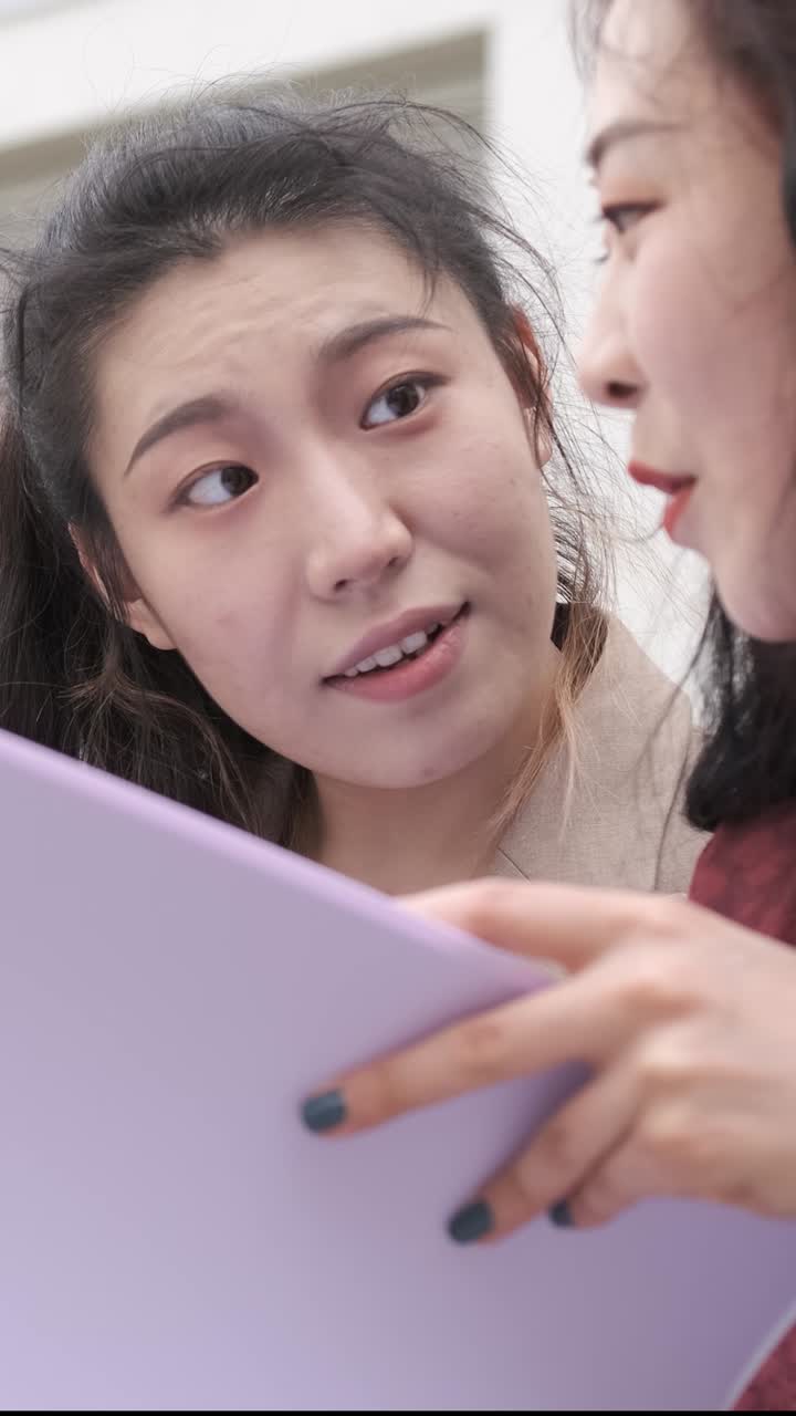 Portrait of two asian girl students talking at break time sitting on campus