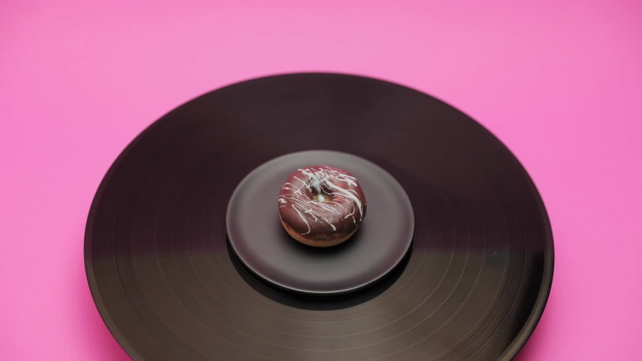 An American donut topped with black chocolate with blue choco lines turns in a circle on a black turntable. The shot from above