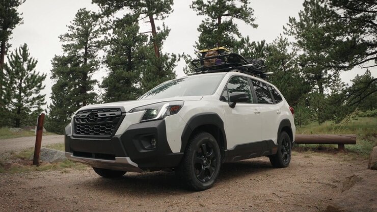 Une voiture avec un coffre de toit rempli d'équipement de camping recule dans un emplacement de camping boisé