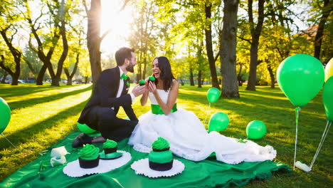 a happy couple playfully enjoys green cupcakes in a sunny park