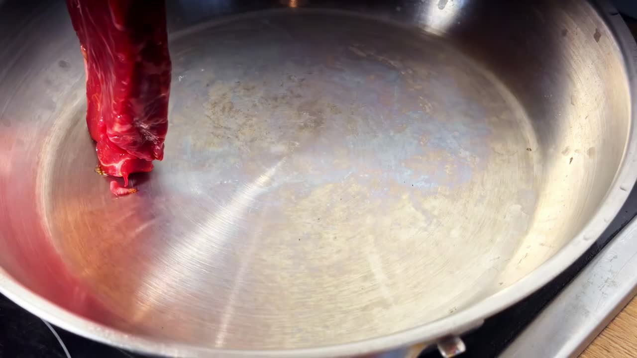 Un taglio fresco di manzo crudo viene messo in una padella calda in acciaio inossidabile, iniziando il processo di rosolatura - Primo piano