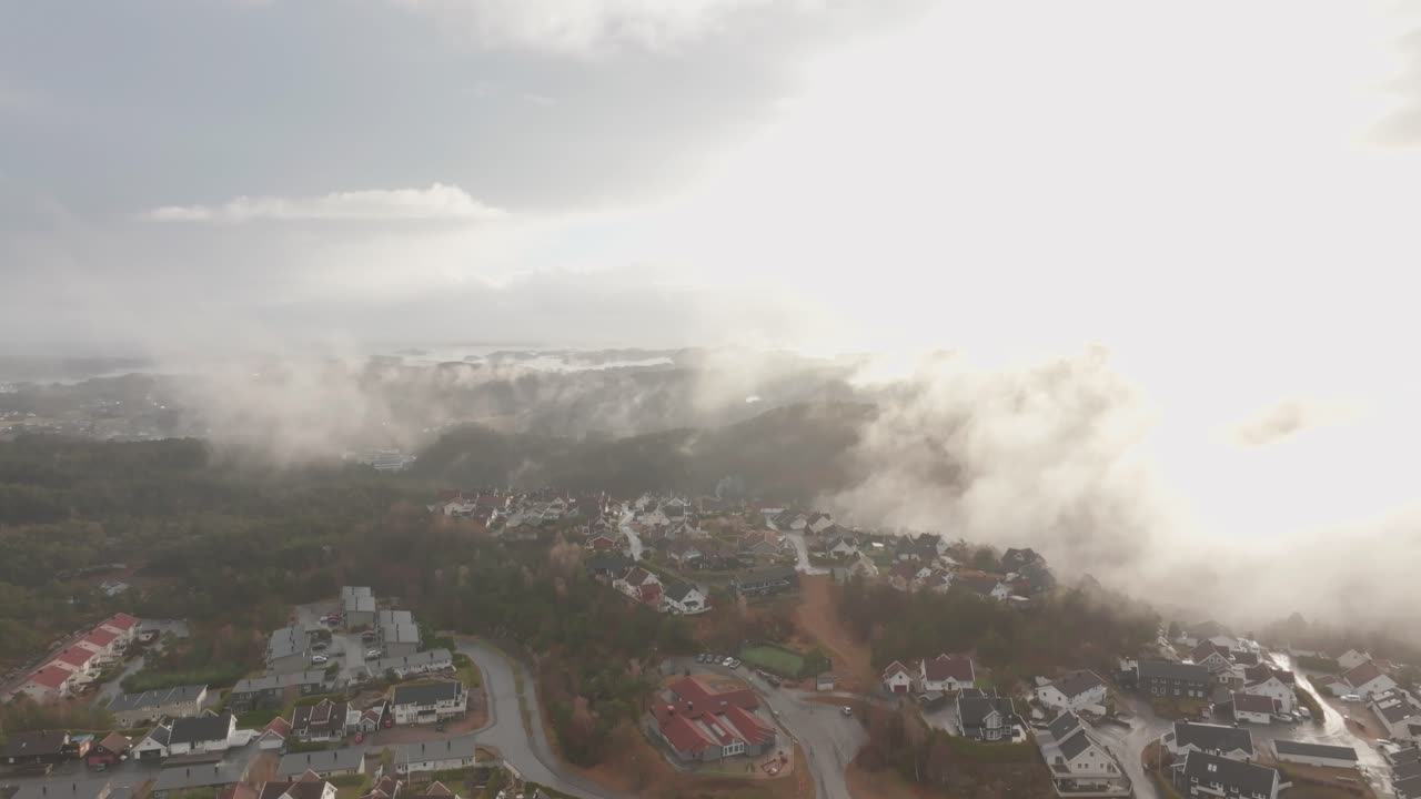 imágenes de drones de una urbanización en noruega con algo de niebla flotando en el aire y el sol iluminando las nubes