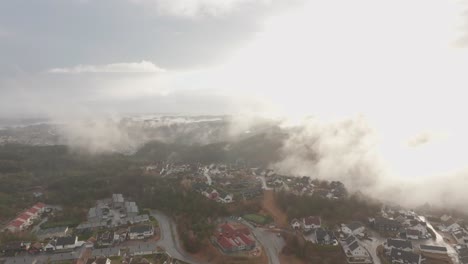 imágenes de drones de una urbanización en noruega con algo de niebla flotando en el aire y el sol iluminando las nubes