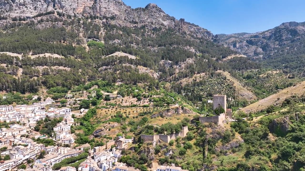 Veduta aerea su appartamenti densamente popolati di Cazorla, Jaén, verso una ripida cresta e il Castello de la Yedra, l'antico castello che domina la cittadina. Sullo sfondo, strati di pini che salgono sui pendii.