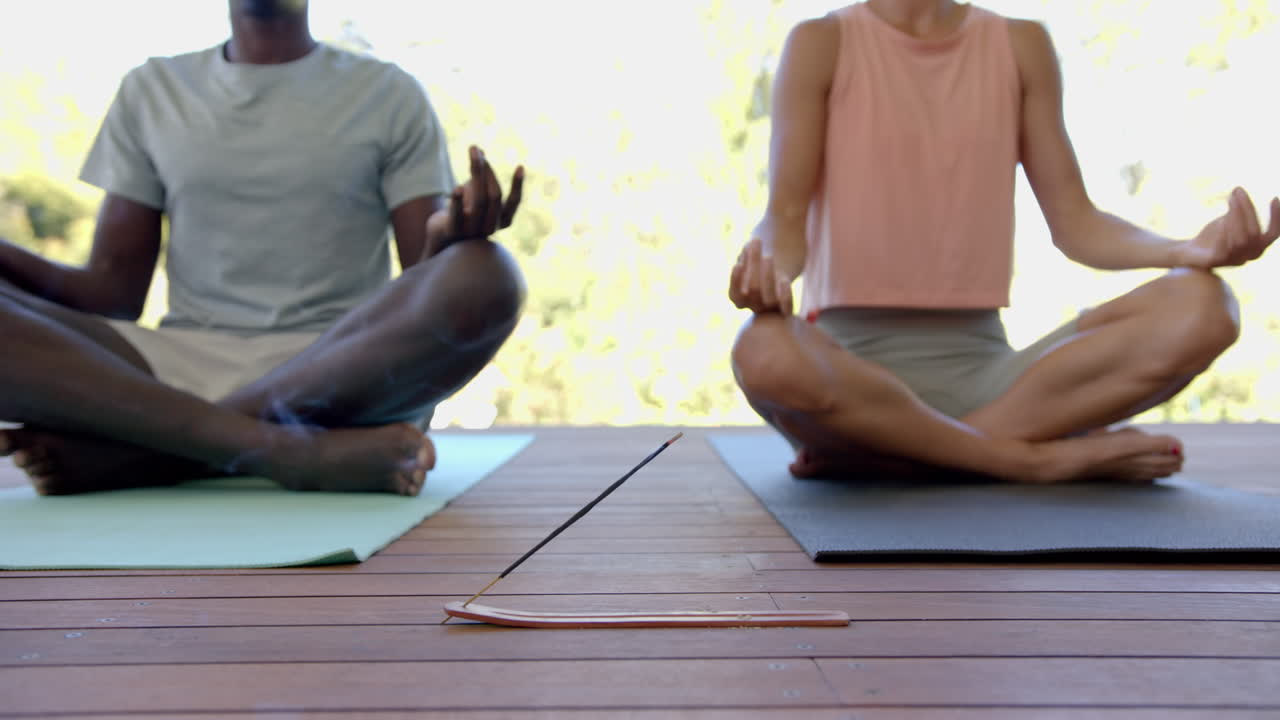 Meditating on yoga mats, diverse couple practicing mindfulness and relaxation outdoors