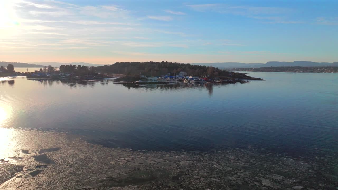 Hovedøya island Hovedoya Aker Brygge Lindøya aerial drone Norway Norge Sunset on horizon harbor ferry boat Norwegian Oslo Fjord frozen ice icy coastline sea calm peaceful salt water upwards motion