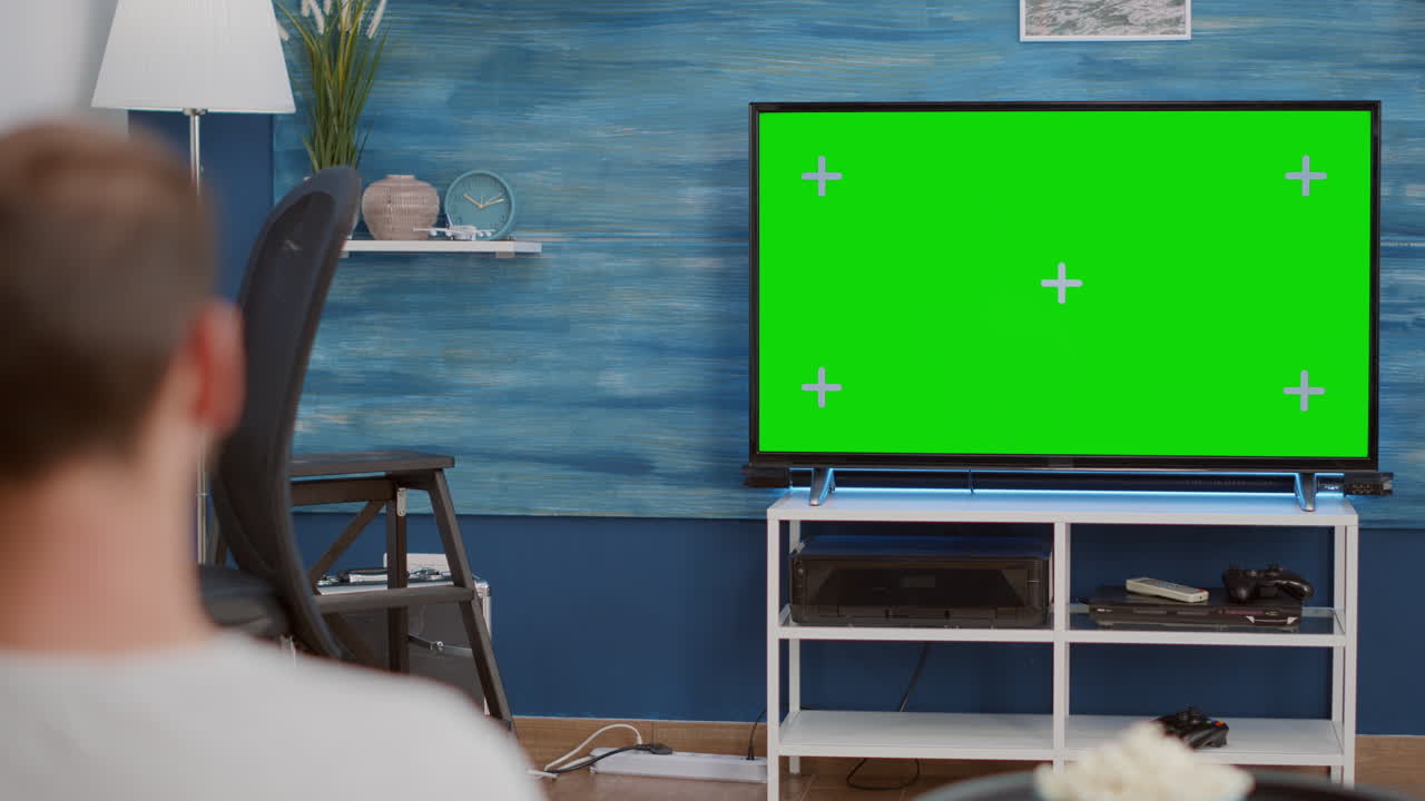 Over shoulder view of man watching movie on tv with green screen relaxing with bowl of popcorn