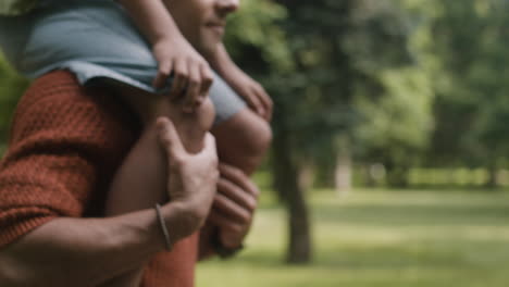 father carrying daughter on shoulders in park