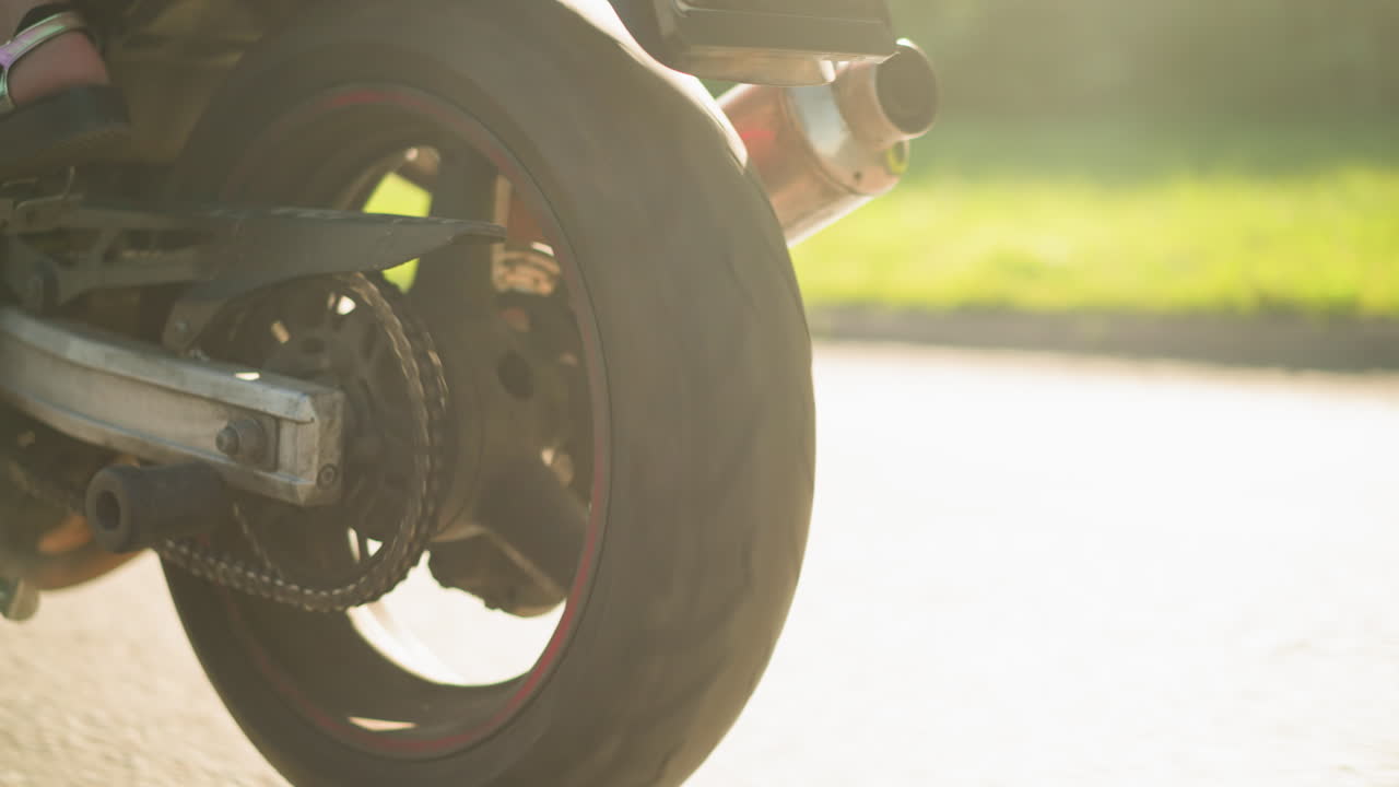 Close-up leg view of two women riding a power bike with one wearing sandals and the other in sneakers, the bike wheels are in motion, and sunlight reflects off the grass along the road
