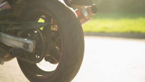 close-up leg view of two women riding a power bike with one wearing sandals and the other in sneakers, the bike wheels are in motion, and sunlight reflects off the grass along the road