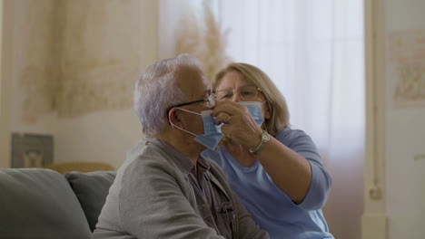 Side-view-of-woman-putting-on-protective-mask-on-husband-at-home