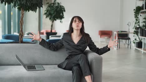 young-frustrated-woman-is-sitting-on-the-couch-in-the-business-center's-lobby-with-a-laptop,-visibly-upset-and-clutching-her-head