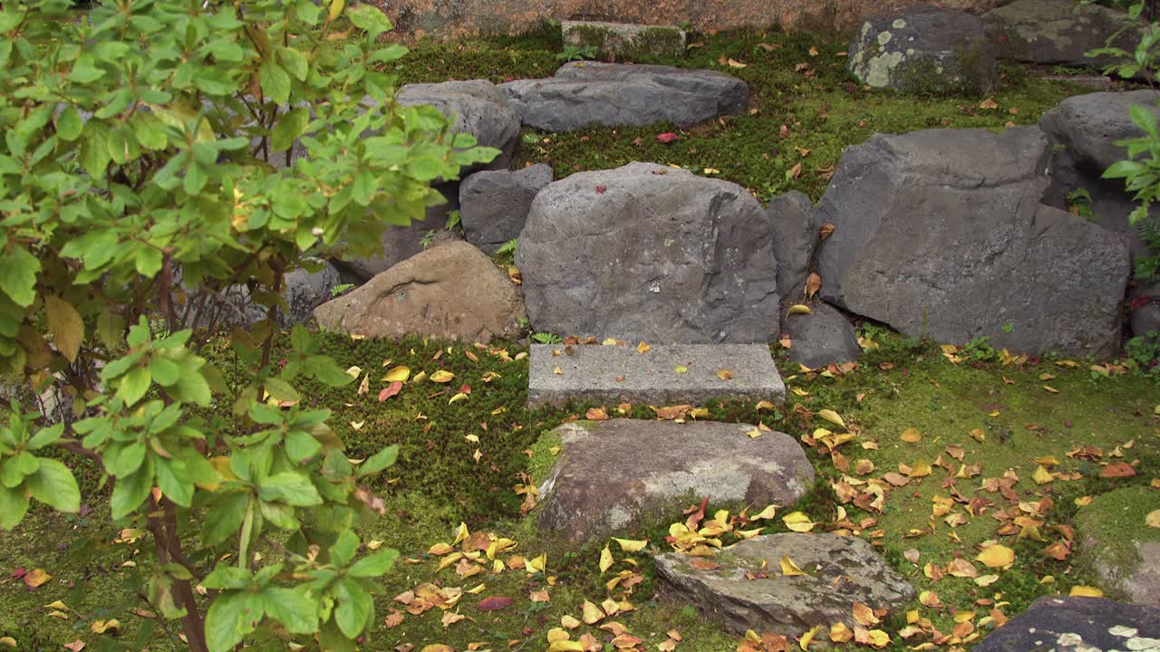 Camera tilts up stone path to big boulder etched with Kanji characters