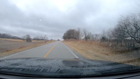 pov thru the windshield and active windshield wipers during a light rain while driving on a county road in rural illinois