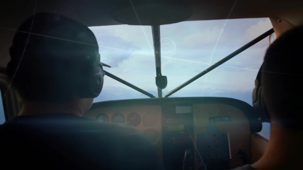 Pilot initiating bank to follow ridge in aviation, co-pilot checking gauges, sunlight streaking