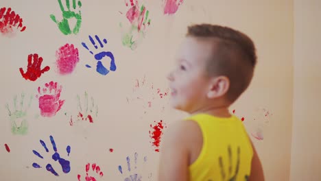 happy mother and her cute boy having fun together leaving their colorful handprints on the wall. young happy family. mother and child concept