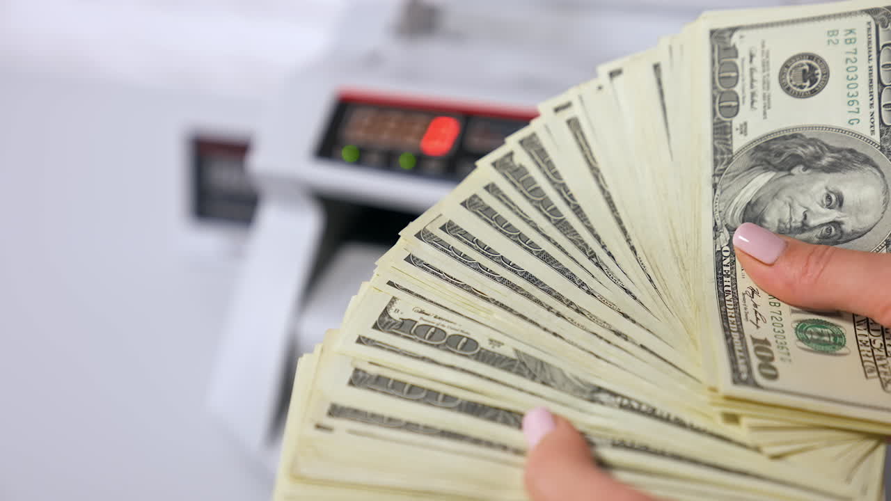 Dollar banknotes in woman's hands. Woman holding a large sum of money on the blur background of electronic counter machine. Close-up. Bank and finance.