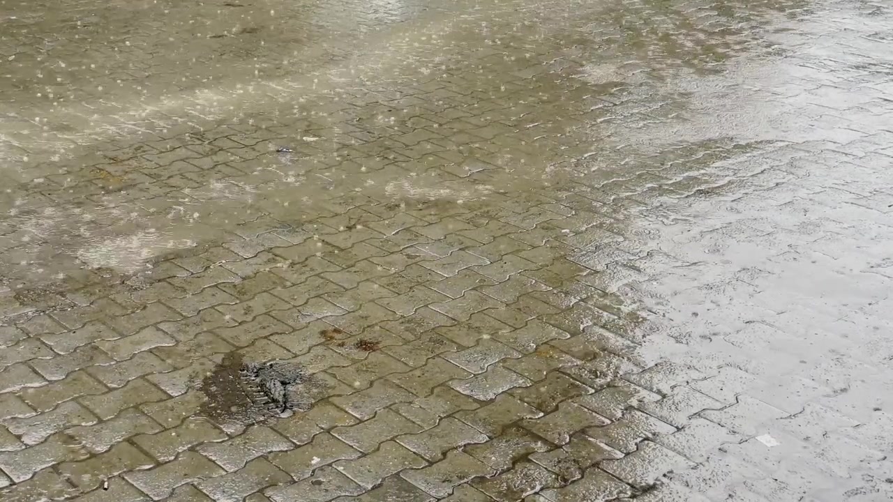 Close up of raindrops hitting shallow puddles across wet interlocking brick pavement during a heavy monsoon shower