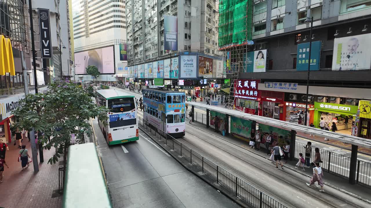 Timelapse view in Causeway Bay, Hong Kong, featuring trams and buses navigating through heavy traffic with vibrant city life and towering skyscrapers in the background.