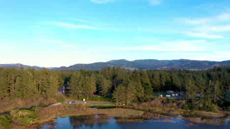 Drone-flying-over-Floras-Lake-in-Langlois,-Oregon,-ascending-and-revealing-pine-trees-and-mountains-in-the-background