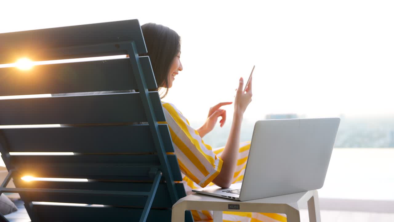 여름날 라이프 스타일 아시아 여성은 럭셔리 수영장 근처에서 휴식을 취하고 차가워합니다. 아시아 여성은 스마트폰에서 앱을 사용하고 노트북에서 이메일을 확인합니다.