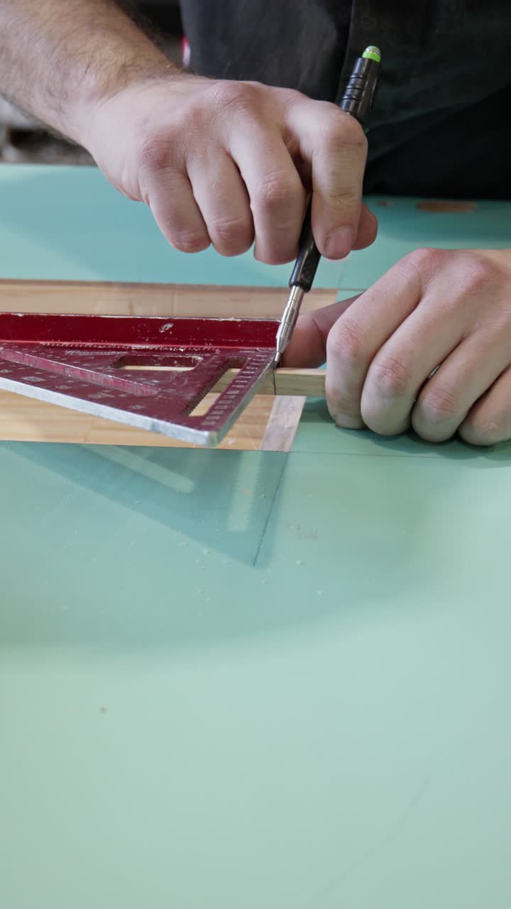 Close-up vertical shot of a carpenter using a speed square and mechanical pencil to mark a precise cut line on a wooden piece. The craftsman carefully aligns the square along the edge