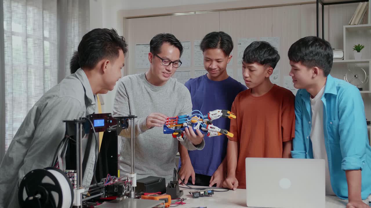 hombre asiático con una computadora portátil e impresión 3d explicando cómo usar una mano cyborg a los niños en la escuela