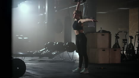 in slow motion a woman lifts a dumbbell over her head while working out in a dark gym. athletic strong woman performs a difficult workout with lifting dumbbells