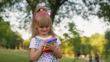 Niña-Pequeña-Y-Elegante-Jugando-Coloridas-Burbujas-De-Silicona-Blandas-Sensorial-Pop-It-Juego-De-Juguete-En-El-Parque