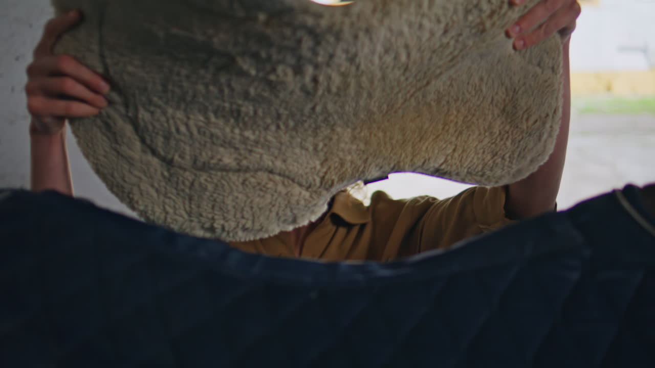 Calm equestrienne saddling horse before ride barn closeup. Jockey putting saddle