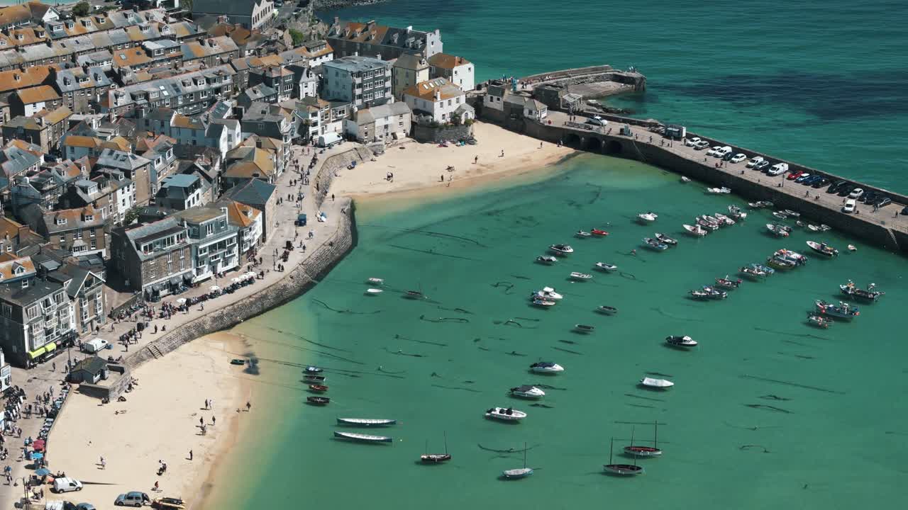 Angled orbit above coastline and harbor of St. Ives, Cornwall England with boats anchored in water