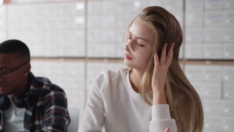 mujer rubia arregla el cabello suelto contra los casos de índice de tarjetas. estudiante cansado de aprender cierra los ojos sentado en la mesa en la biblioteca de la universidad. exceso de trabajo durante la preparación
