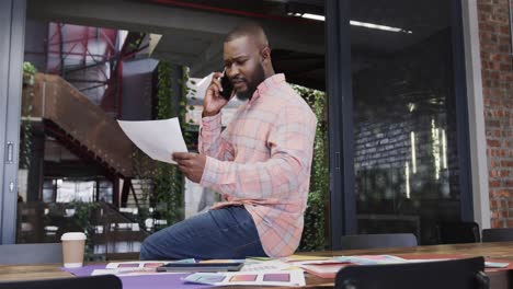 african american casual businessman with document talking on smartphone sitting on desk, slow motion