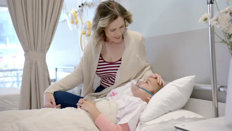 caucasian mother comforting daughter patient in oxygen mask lying in hospital bed, slow motion