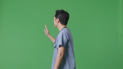 side view of asian male doctor with stethoscope waving hand and smiling while walking on green screen background in the hospital